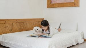 a young girl reading a book with a dog on a bed at Chuncheon Remember Pet Pension in Chuncheon