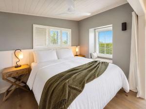 a bedroom with a large white bed and two windows at Smiths Cottage - Stay Waiheke in Oneroa