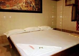 a bed with two white sheets and a picture on the wall at Olive inn in Kanyakumari