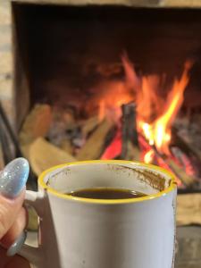 a person holding a cup of coffee in front of a fire at Alpine Lodge Bakhmaro in Chʼkhakoura