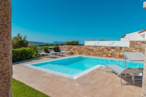 a swimming pool with chairs and a stone wall at VILLA INDIPENDENTE AL MARE BUDONI in Tanaunella