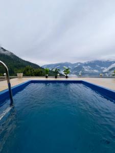 a large blue swimming pool with mountains in the background at SaffronStays Interstellar in Manāli