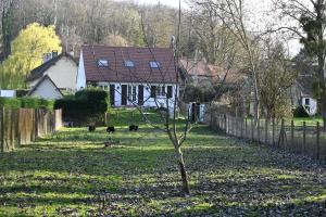 a tree in a field with a fence and a house at Cottage des Moutons Espiègles in Saint-Martin-de-Nigelles