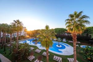 a resort with a pool and palm trees and chairs at Estival Isla Cristina in Isla Cristina