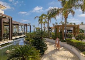 a woman walking through a resort with a pool at Olympic Lagoon Resort Paphos in Paphos