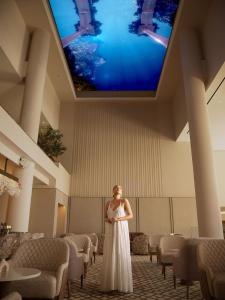 a woman in a white dress standing in a room with a large screen at Olympic Lagoon Resort Paphos in Paphos +74 photos