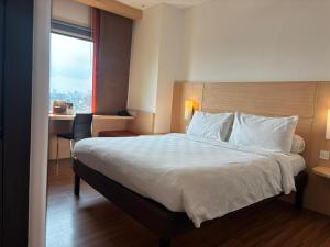 a bedroom with a bed with a desk and a window at Swiss-Belinn Cawang in Jakarta