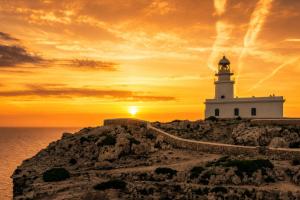 a lighthouse on a cliff with the sunset in the background at Kampaoh Menorca in Cala Galdana