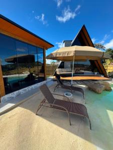 a patio with two chairs and an umbrella in the water at Chalé lago Azul in Venda Nova do Imigrante