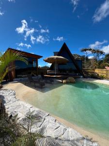 a house with a swimming pool with chairs and an umbrella at Chalé lago Azul in Venda Nova do Imigrante