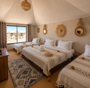 a bedroom with three beds and a large window at Sinbad Merzouga Camp in Merzouga