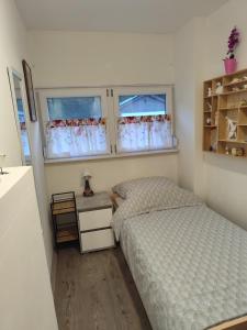 a small bedroom with a bed and two windows at Niki Vendégház in Abaliget