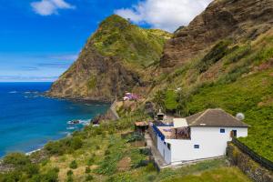 a white building on a hill next to the ocean at Maiata Beach House 1 in Porto da Cruz