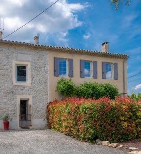 a stone house with blue windows and a hedge at Charme au cœur des vignes in Malras