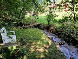 a white bench sitting in the grass next to a stream at Maison d'hôtes La Cerisaie in Breitenbach