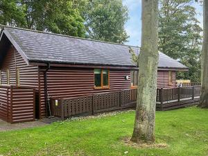 a wooden cabin with a fence and a tree at Sycamore Lodge in Sewerby
