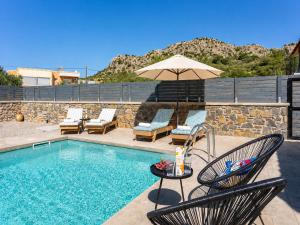 a swimming pool with chairs and an umbrella and a table at La Casa Di Pietre 3 in Kiotari