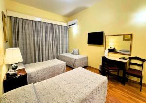 a hotel room with two beds and a desk at Dayrell Hotel e Centro de Convenções in Belo Horizonte