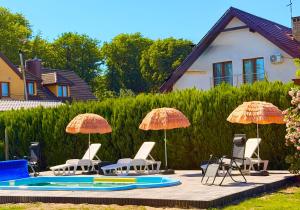 a group of chairs and umbrellas next to a pool at Złote Piaski Pensjonat z basenem in Darłowo