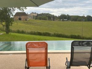 two chairs sitting next to a pool with an umbrella at Gîte Les Jacquets in Hautefort