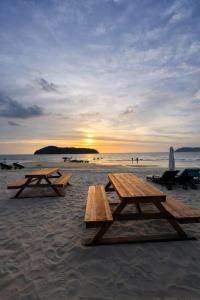 two picnic tables on the beach with the sunset in the background at Seaside Dorm Cenang in Pulau Tepur