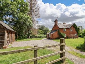 an old brick house with a fence in front of it at Wolvesacre Mill Cottage in Whitchurch