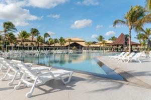 a pool at a resort with white chairs and palm trees at Vila Galé Resort Cumbuco - All inclusive in Cumbuco