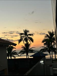 a sunset from the balcony of a house with palm trees at Apto Sol Nascente in Mongaguá