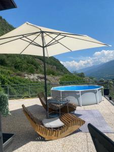 a table and chairs under an umbrella next to a swimming pool at casa vacanze LA CA Del Cunfec in Sondrio