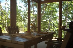 a table in a screened in porch with a view of trees at Refuge du Cap in Baie-Saint-Paul