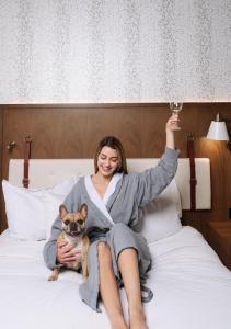 a woman sitting on a bed with a dog and a glass of wine at Hyatt Centric Downtown Denver in Denver