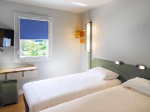 a hotel room with two beds and a window at Ibis Budget Sallanches in Sallanches