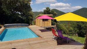a deck with a pool and a yellow umbrella and chairs at Au Royaume des Chats in Soudorgues
