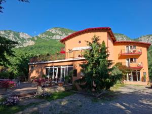 a building with a tree in front of it with mountains at Pensiune Safrane in Băile Herculane