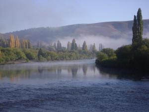 a view of a river with trees and fog in the distance at Cabañas El Puente Azul in Aluminé