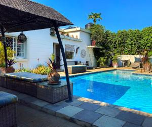 a swimming pool with an umbrella next to a house at Guesthouse MALAGUETA INN II in Maputo