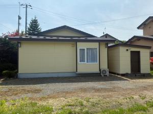 a small yellow house with a driveway at Private Rock Onsen Villa Orin & Zen Garden in Shiraoi