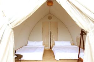 two beds in a tent with white sheets at NSH Riverside Glamping Resort in Hanoi