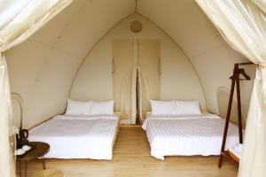two beds in a tent with white sheets at NSH Riverside Glamping Resort in Hanoi