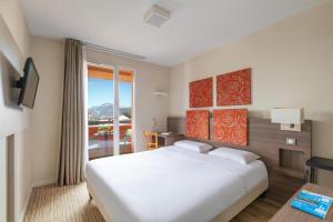 a bedroom with a large white bed and a window at Kyriad Chambéry Centre - Hôtel et Résidence in Chambéry