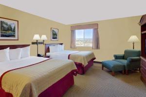 a hotel room with two beds and a chair and a window at Pinedale Hotel & Suites in Pinedale