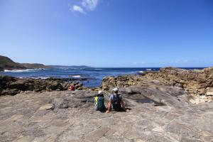 two people sitting on the rocks near the ocean at Fogar dos Americanos in Borneiro