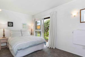 a white bedroom with a bed and a window at Beachfront Marine Parade in Mount Maunganui