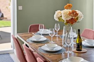 a wooden table with a vase of flowers and wine bottles at CHERRYTREES Beautiful 5 Bedrooms, Sleeps 9, 3 Bathrooms, Parking, Ideal for Groups and Work Stays in Corby +34 photos