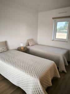 two beds in a white room with a window at A Quinta in Vila Nova de Milfontes