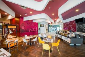 a restaurant with tables and yellow chairs and a counter at favehotel Pluit Junction in Jakarta