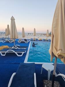 a man swimming in a pool with chairs and umbrellas at Modern Hotel-Style Apartment in El Alamein