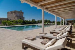 a row of chaise lounge chairs next to a swimming pool at Masseria Donna Menga - The Leading Hotels of the World in Torre Lapillo