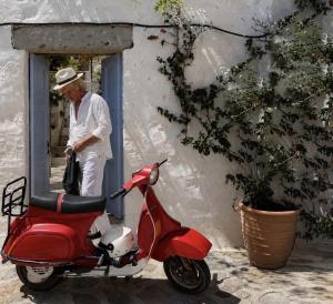 a man standing in a window next to a red scooter at Chora Heritage Residence by Belle-Stay in Patmos