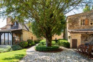 a stone house with a tree in the yard at La Maison des Sarrasins in Beynac-et-Cazenac